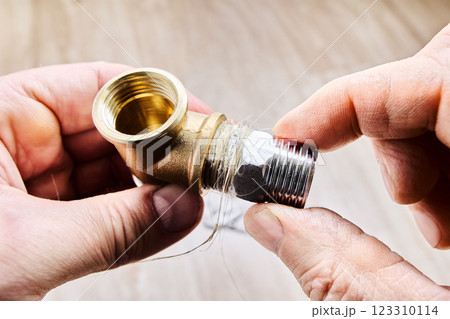 Hex nipple barrel reducer adapter is being sealed with plumbing hemp and screwed into brass elbow fitting, ensuring secure threaded joint in pipe fitting. 123310114