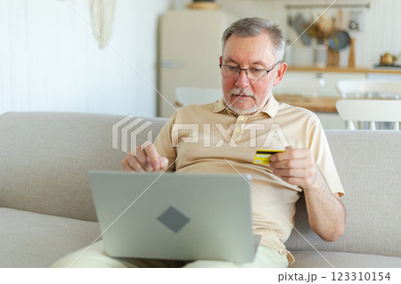 Senior man shopping online using laptop paying with credit card. Old grandfather buying on Internet enter credit card details. Online shopping delivery service. Older generation modern tech usage 123310154