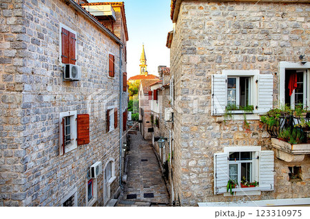 A charming stone alley in the ancient European town of Budva at sunset with a church spire in the distance. 123310975