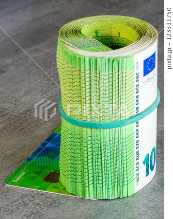 A thick roll of green 100 euro banknotes tied with a rubber band placed on a business payment card 123311750