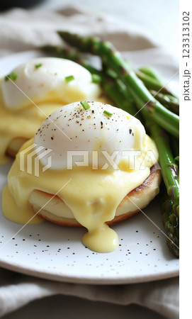 elegantly plated eggs benedict with poached eggs, hollandaise sauce, toasted english muffins, fresh asparagus, rustic linen napkin, neutral textured background 123313102
