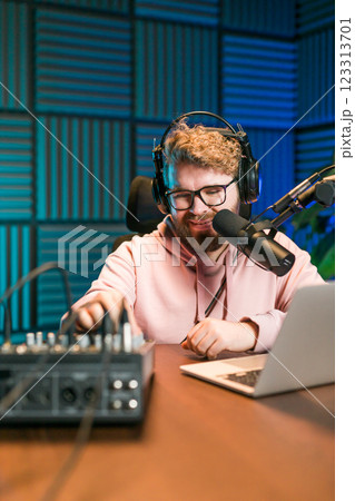 Cheerful young man recording podcast in studio. Confident man with headphones and microphone recording a podcast. Happy guy talking on web radio. 123313701