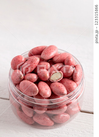 Chocolate-covered nuts on a white wooden background. Candies in a clear glass jar. Chocolate-covered nuts on a white wooden background. Candies in a clear glass jar. 123315866