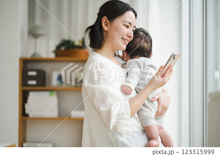 赤ちゃんを抱っこしながらスマホを見る女性 赤ちゃんを抱っこしながらスマホを見る女性 123315999