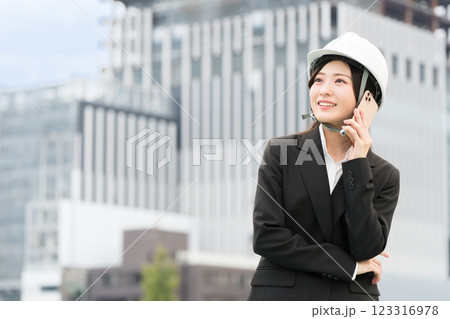 スーツにヘルメットを被ってスマホで通話する若い女性 施工管理者 現場監督 土木女子(ドボジョ) スーツにヘルメットを被ってスマホで通話する若い女性 施工管理者 現場監督 土木女子(ドボジョ) 123316978