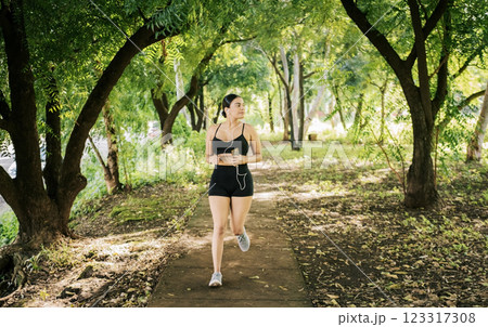 Lifestyle of sporty young woman running in a park surrounded by trees. Healthy lifestyle concept, Sporty young woman running in a park. A girl running in a park while listening to music Lifestyle of sporty young woman running in a park surrounded by trees. Healthy lifestyle concept, Sporty young woman running in a park. A girl running in a park while listening to music 123317308