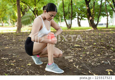 Athlete woman with knee muscle pain. Athlete girl on the ground with knee pain outdoors. Runner woman with knee pain outdoors. Athlete knee pain and fractures concept 123317321