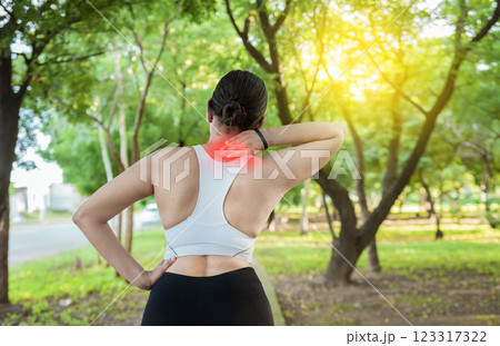 Running woman with shoulder muscle pain in a park. Shoulder pain concept of a runner athlete. Athlete girl in pain rubbing her shoulder outdoors. Back view of sporty woman with shoulder pain 123317322