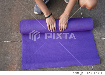 Woman hands rolling up the mat outside. Athlete woman's hands rolling up the mat after exercising. Concept of rolling up mat after exercise 123317331
