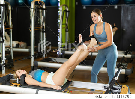 Female trainer helps to do leg exercises on the reformer Female trainer helps to do leg exercises on the reformer 123318790