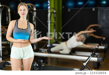 Female trainer stands in gym against background of Pilates reformer machines 123318854