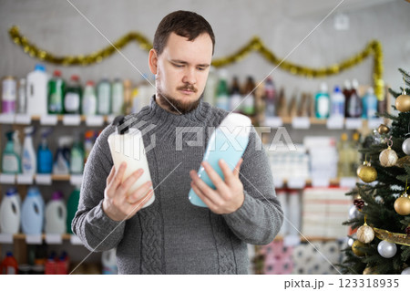 Happy handsome man choosing shampoo or shower gel in cosmetics store decorated for New Year holiday Happy handsome man choosing shampoo or shower gel in cosmetics store decorated for New Year holiday 123318935