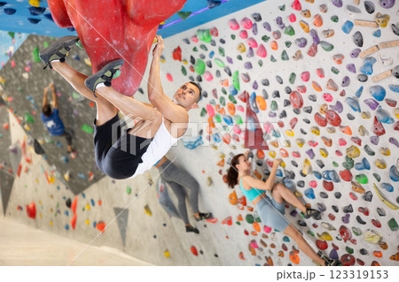 Young man and two women engaged in rock-climbing in indoor hangar Young man and two women engaged in rock-climbing in indoor hangar 123319153
