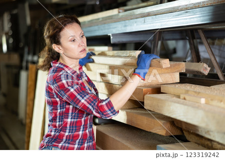 Woman employee of carpentry workshop takes out necessary board from stack of materials Woman employee of carpentry workshop takes out necessary board from stack of materials 123319242