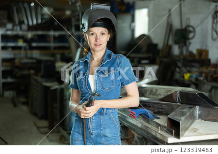 Portrait of a female welder standing with a welding semi-automatic machine and a safety helmet in metal machining workshop 123319483