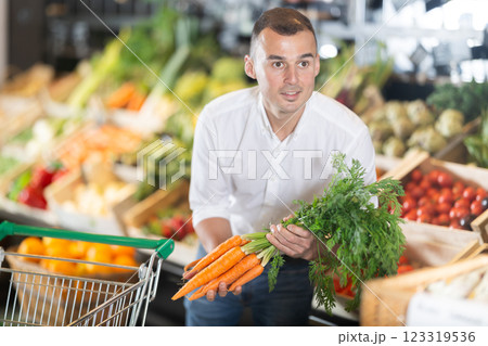 In vegetable department of bio supermarket, male customer took bunch of carrots from window 123319536