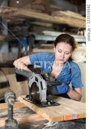 Working at sawmill - woman saws wooden board using circular saw 123319542