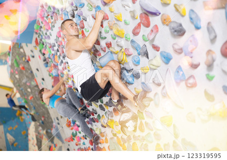 Young man climbing on artificial rock wall in rock-climbing gym 123319595