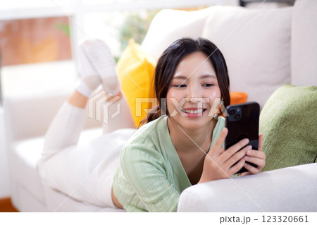 Young asian businesswoman looking smartphone smiling and relax lying on sofa in living room. 123320661