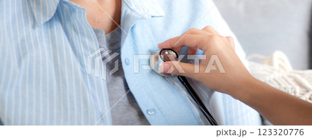 Caregiver young nurse woman examining elderly with stethoscope for checkup sitting on sofa. 123320776