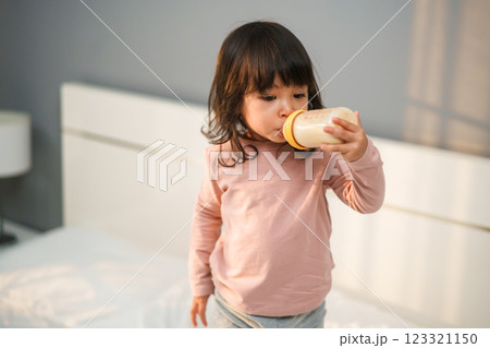 toddler girl drinking milk from bottle on bed 123321150