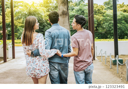 Unfaithful girl walking in the park with her boyfriend while holding another man hand. Love triangle concept. Woman holding hands with another man while walking with her boyfriend outdoor Unfaithful girl walking in the park with her boyfriend while holding another man hand. Love triangle concept. Woman holding hands with another man while walking with her boyfriend outdoor 123323491