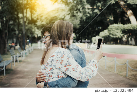 Cheating girlfriend hugging boyfriend and looking at cell phone. Unfaithful woman looking at cell phone while hugging boyfriend. Girl addicted to cell phone hugging boyfriend Cheating girlfriend hugging boyfriend and looking at cell phone. Unfaithful woman looking at cell phone while hugging boyfriend. Girl addicted to cell phone hugging boyfriend 123323494