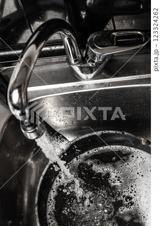 Black and white: water flowing from tap into a dirty pan in the sink. Foamy soap and close up shot. Everyday household chore 123324262