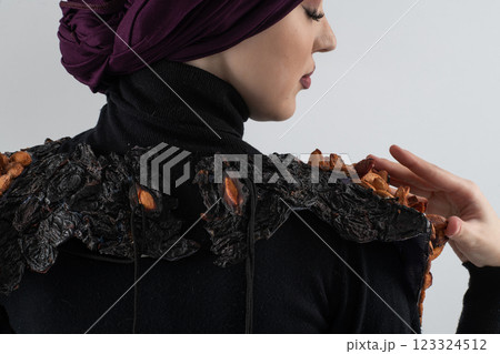 A stylish Muslim woman in a hijab presents her innovative handmade fashion accessory crafted from dried plums in a professional studio. A stylish Muslim woman in a hijab presents her innovative handmade fashion accessory crafted from dried plums in a professional studio. 123324512