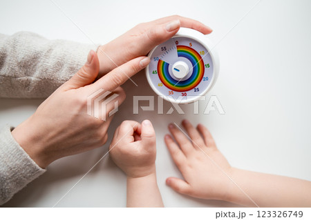 Adult and child hands adjusting colorful kitchen timer on white surface Adult and child hands adjusting colorful kitchen timer on white surface 123326749