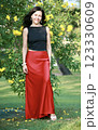 Beautiful brunette woman 51 years old in a satin red long skirt posing against the background of a flowering tree in Goa India 123330609