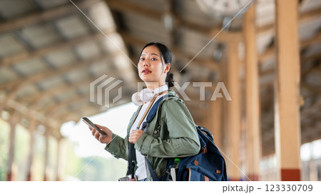 An asian woman is looking around while holding phone, standing in train station or railway station. An asian woman is looking around while holding phone, standing in train station or railway station. 123330709