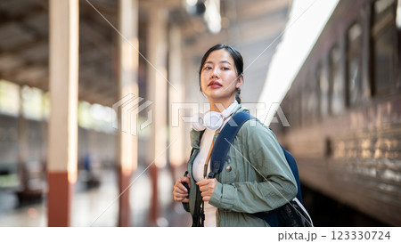 An asian woman is looking ahead while holding bag straps, standing alone on station platform. An asian woman is looking ahead while holding bag straps, standing alone on station platform. 123330724