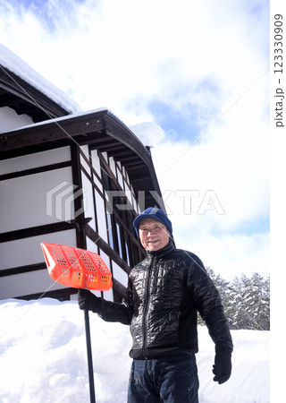 雪国で雪はねを使用して除雪をしている笑顔の老人 123330909