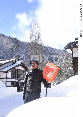 雪国で雪はねを使用して除雪をしている笑顔の老人 123330912