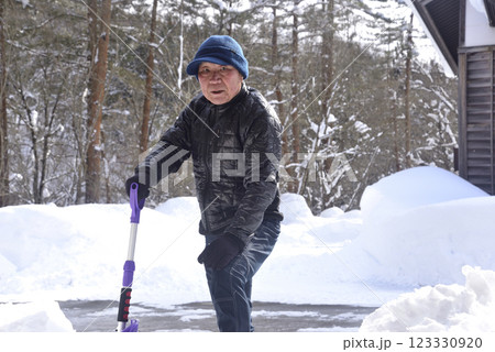 雪国で雪はねを使用して除雪をしている笑顔の老人 123330920