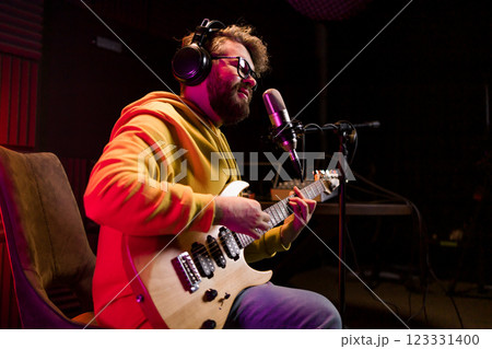 Man vocal artist singing in a recording studio with guitar. Male singer singing a song and playing guitar. Sound record and music streaming concept Man vocal artist singing in a recording studio with guitar. Male singer singing a song and playing guitar. Sound record and music streaming concept 123331400