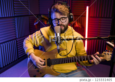Man vocal artist singing in a recording studio with guitar. Male singer singing a song and playing guitar. Sound record and music streaming concept Man vocal artist singing in a recording studio with guitar. Male singer singing a song and playing guitar. Sound record and music streaming concept 123331405