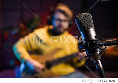 Male singer recording songs by using a studio microphone and and playing guitar in a music recording studio. Performance and show in the music business, streaming and recording music. 123331620