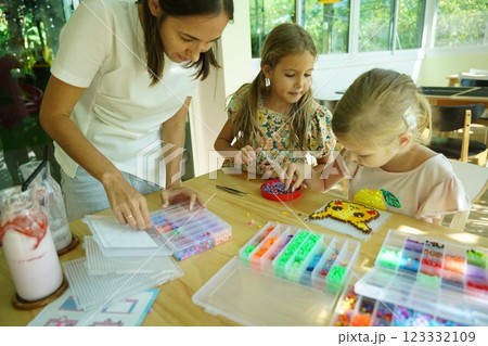 Teacher in workshop teched two girls how to assemble a thermo mosaic Teacher in workshop teched two girls how to assemble a thermo mosaic 123332109