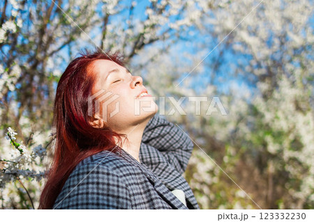 Beautiful red-haired woman enjoying smell in a flowering blooming spring garden. Spring blossom. Copy space 123332230