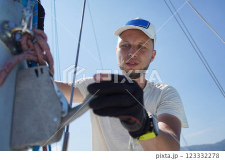 Male captain on deck of sailboat opening sails pulling the rope 123332278