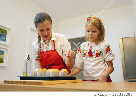 Mother and daughter in the kitchen in traditional Ukrainian costumes making cupcakes for Easter Mother and daughter in the kitchen in traditional Ukrainian costumes making cupcakes for Easter 123332295