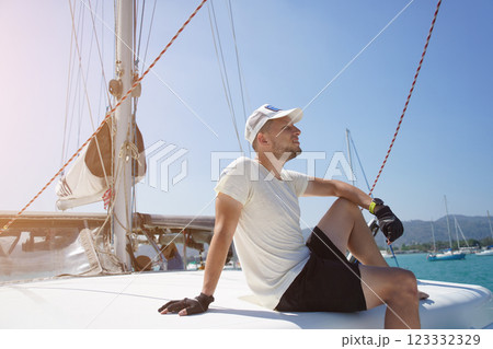 A man is calmly sitting on the deck of a beautiful sailboat A man is calmly sitting on the deck of a beautiful sailboat 123332329