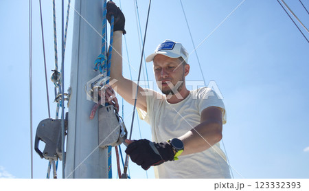 Male captain on deck of sailboat opening sails pulling the rope 123332393