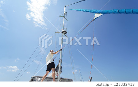 Male captain on deck of sailboat opening sails pulling the rope Male captain on deck of sailboat opening sails pulling the rope 123332415