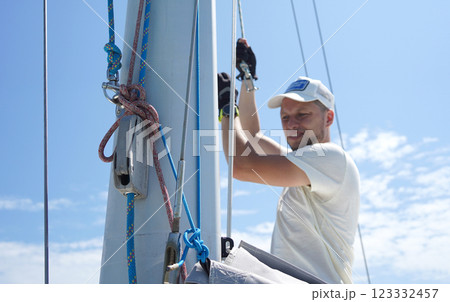 Male captain on deck of sailboat opening sails pulling the rope 123332457