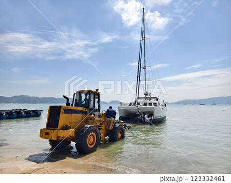 Yellow tractor is pulling a boat out of the water in a beautiful coastal area 123332461