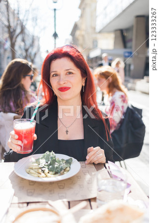 Millennial woman eating italian pasta at restaurant on the street in spring. Concept of Italian gastronomy and travel. Stylish woman with red hair Millennial woman eating italian pasta at restaurant on the street in spring. Concept of Italian gastronomy and travel. Stylish woman with red hair 123333267