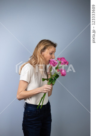 on light gray background a young blonde girl in a light T-shirt in her hands pink peony roses March 8th looks away in a state of shock marriage proposal on light gray background a young blonde girl in a light T-shirt in her hands pink peony roses March 8th looks away in a state of shock marriage proposal 123333689